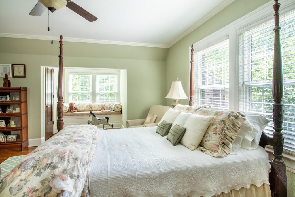 Guest bedroom with floral comforter and pillows in front of an upholstered window seat