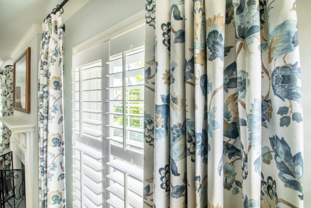 Blue and white floral drapery layered with plantation shutters