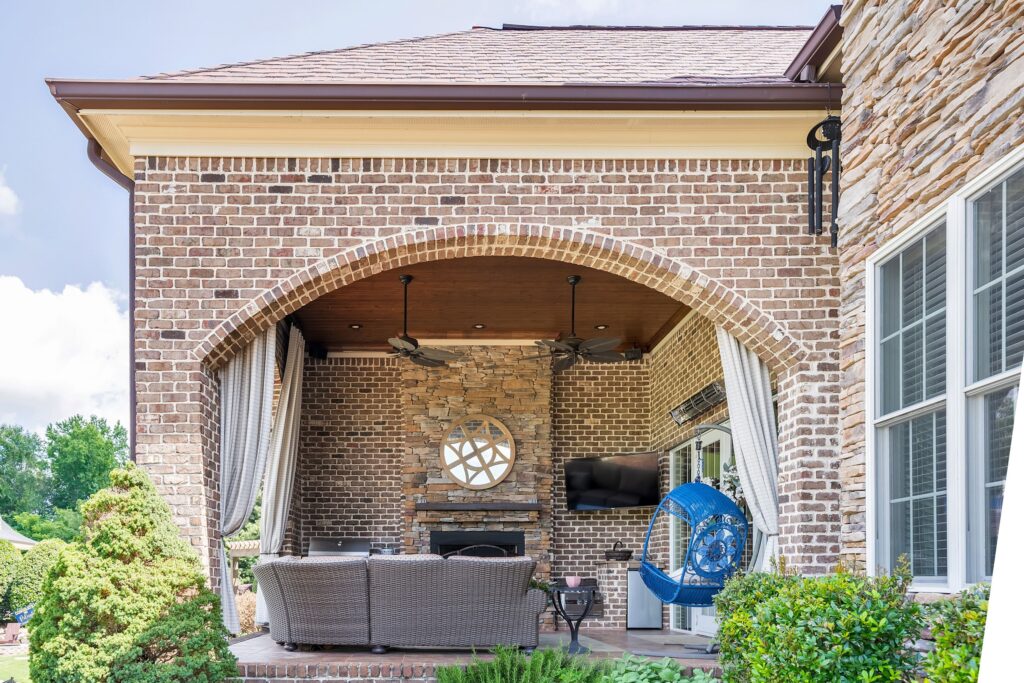 Covered patio with stone fireplace, brick walls, drapery, and wicker sofa 