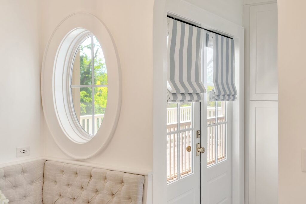 oval window beside exterior doors with striped Roman shades