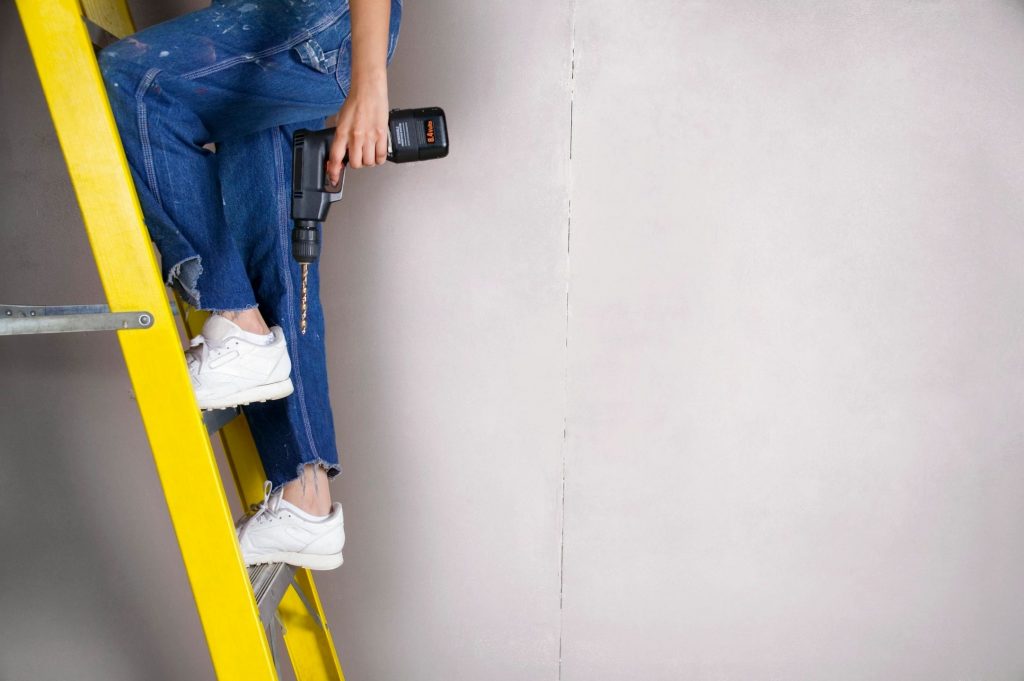 woman climbing ladder with power tool