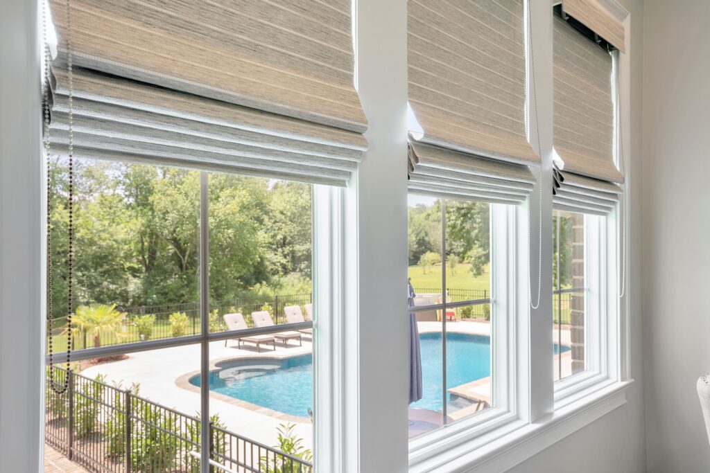 three windows with neutral flat fold roman shades overlooking a pool