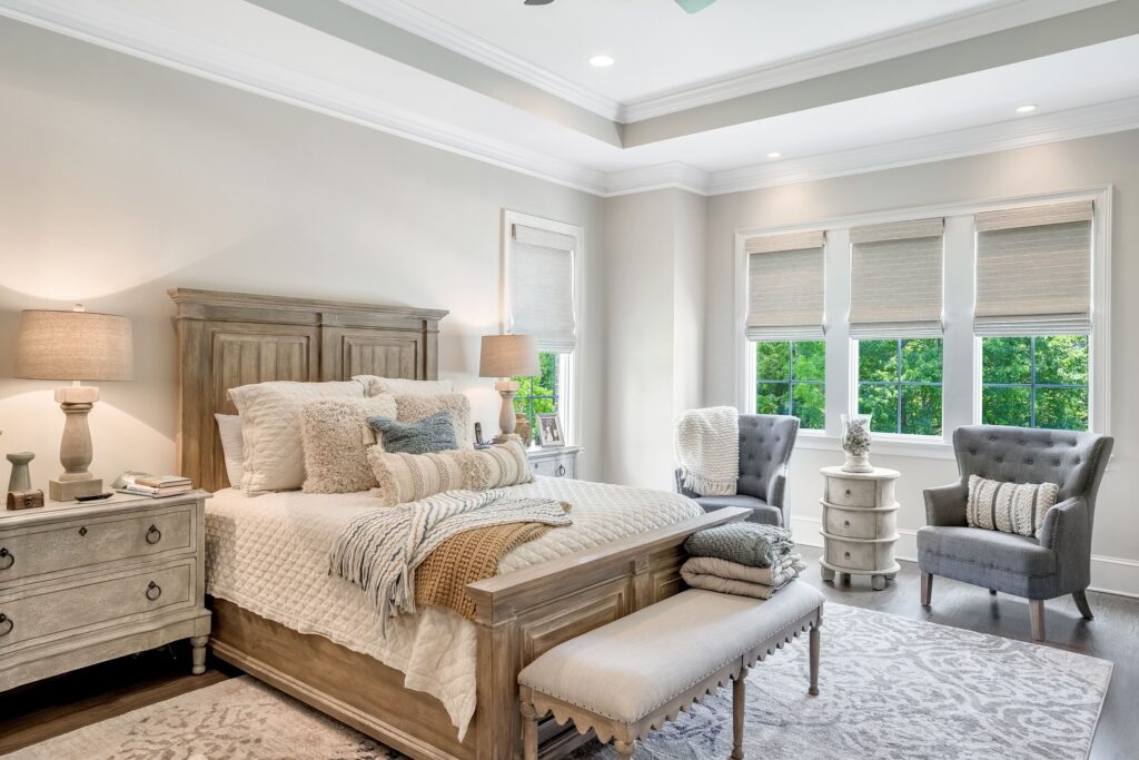 master bedroom with large wooden bed and three windows with neutral roman shades