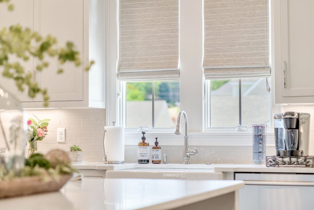 two windows with neutral roman shades over a kitchen sink