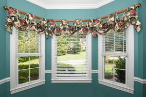 Horizontal blinds and floral top treatments covering bay windows in teal room