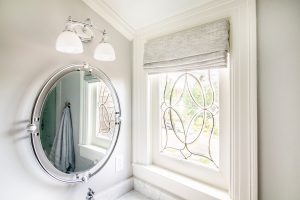 Roman shades covering bathroom window with intricate grille pattern